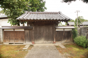 芝生の庭の奥に木造瓦葺の五十嵐家住宅門がある写真