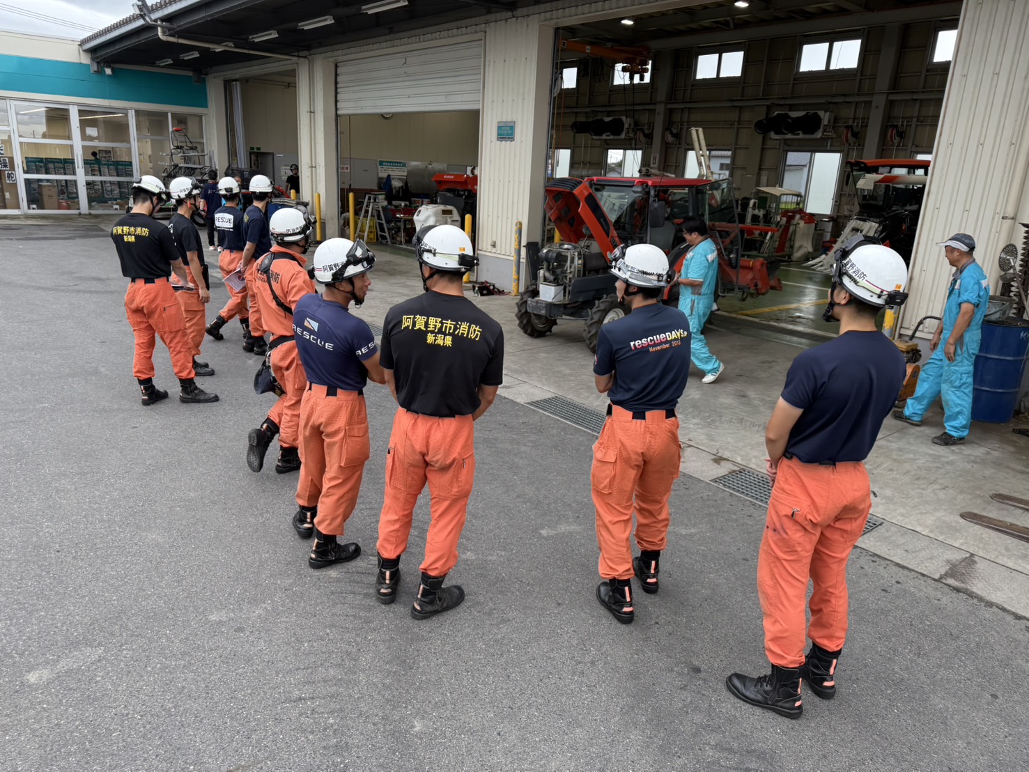 倉庫内で農作業用車両の説明を聞いている10名程の救助隊員の様子
