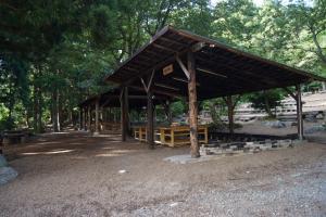 周りにたくさんの木があり、木造の屋根が設置されている野外炊飯場の写真