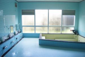 水色のタイル張りで左側にシャワーが設置され、奥にすりガラスの窓、窓の傍に浴槽のある風呂場の写真