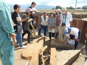遺跡の発掘調査現場で川跡や土器・石器を見学している参加者の写真