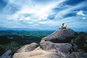 五頭山の岩の上に座って眼下に広がる蒲原平野を眺めている人物の写真