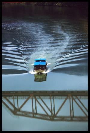川の水面に反射した橋の影に向かって進んでくる遊覧船の写真