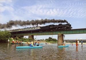 鉄橋を黒い煙を吐きながら走っていくSLを川の中からカヌーに乗って眺めている人々の写真