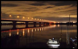 薄暗い中で橋に等間隔に設置された街灯が光って川の水面に映っている写真