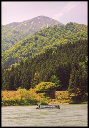 川の中を進む一艘の遊覧船と奥に広がる緑色の山々の写真