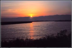 河の向こうの山脈から昇ってくる朝日とオレンジ色に輝いている朝焼けの空の写真