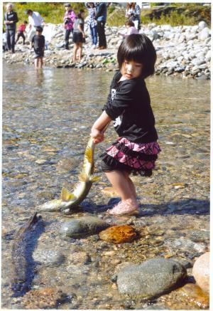 大きな鮭のしっぽをつかみ岸に引き上げようとしている女の子の写真