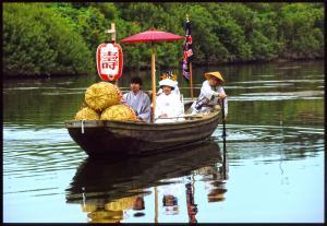 先頭に3つの米俵が乗っている船に着物を着た男性と角隠しに白無垢姿の女性、船をこぐ船頭が乗っている写真