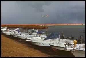 川岸に停泊している何艘もの白いボート、川の上空を飛んでいる白い飛行機の写真