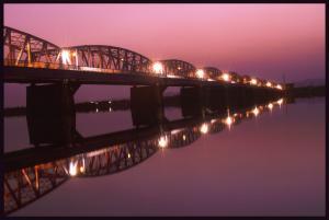 夕暮れ時の薄い紫色の空と等間隔に明かりが灯っている橋が水面にきれいに反射して映っている写真