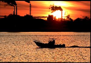 夕焼けと工場を背景に、漁を終えた漁船が帰ってくる写真