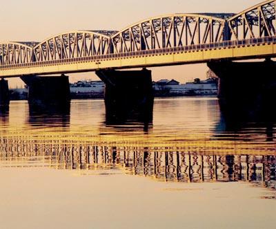 光に当たって黄金色に輝く鉄橋が川の水面に写っている写真