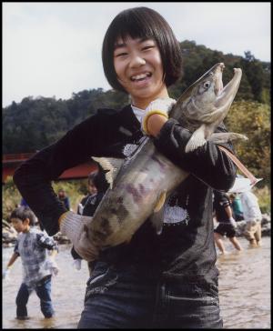 両手で大きな鮭を抱えている笑顔の女性の写真