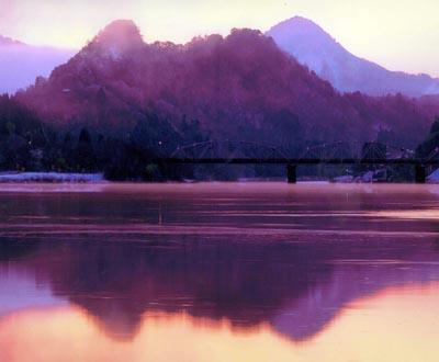 濃い紫と薄い紫のグラデーションが美しい山々が川の水面に映っている写真