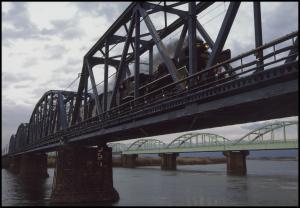 川にかかった鉄橋を走る黒いSL列車の写真