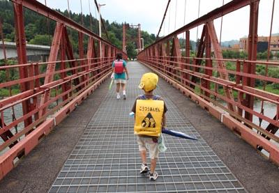 赤い鉄橋を歩いている小学生の女の子と男の子の写真