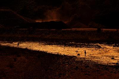 夕焼けが反射してオレンジ色に輝く川で釣りをしている人々の写真