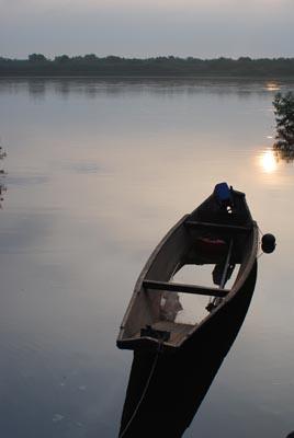 川に浮かんでいる1艘の船と水面に太陽の光が写っている写真
