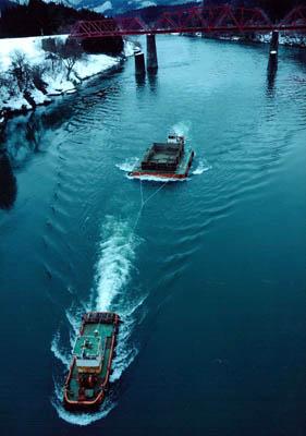 はしけを引っ張って阿賀野川を進んでいく船と川にかかる赤い鉄橋の写真