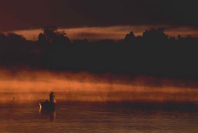 霧が立ち、水面がオレンジ色に輝いている川に人が乗っている一艘の船が写っている写真
