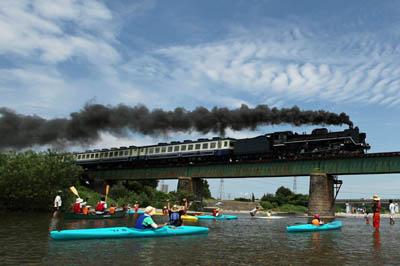 鉄橋を黒煙を吐き出しながら走っていくSLに向かって、カヌーに乗ったまま手を振っている人々の写真