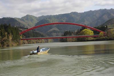 川にかかる赤い鉄橋と船が進んだあとの水面が緩やかに波打っている川の写真