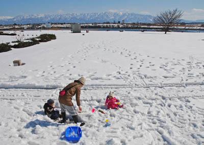 雪が積もった公園で遊んでいる母親と2人の子供たちの写真