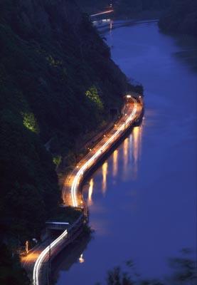 阿賀野川沿いの道路を走っている車のライトが川の水面に映って輝いている写真