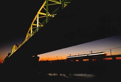 夕闇の中、ライトアップされて黄色く光っている鉄橋の写真