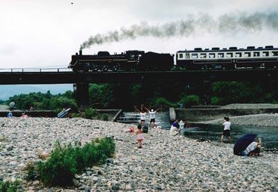 煙を吐きながら鉄橋を走っていくばんえつ号と列車に向かって手を振る子供たちの写真