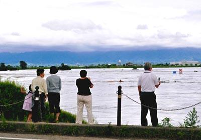 増水した阿賀野川を土手から見ている人々の写真