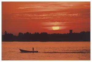 沈みかけの太陽とオレンジ色の空と川、川の中に一艘の船と人物のシルエットが写っている写真