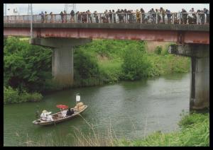 船に乗って川を進む新郎新婦を橋の上から眺めているたくさんの人々の写真