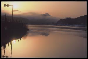 山の向こうに朝日が昇り空が金色に輝き、川の水面も光が反射している写真