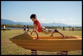 ボートの形をした遊具の前後についているアーチ状の持ち手に両手と両足をのせて浮いているような格好で遊んでいる男の子の写真