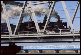 鉄橋を白い煙を吐き出しながら走っていくSL列車の写真