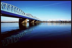 濃い青と水色のグラデーションの空と川、川にかかっている鉄橋の写真