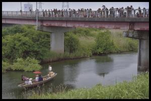 船に乗って川を進む新郎新婦を橋の上から大勢の人が眺めている写真