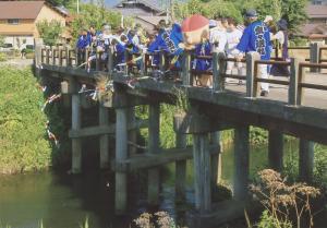 青い法被を着た人々が橋の上から五色旗を流している写真