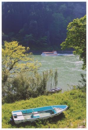 阿賀野川を進んでいく遊覧船イザベラバードと川岸に置かれている一艘のボートの写真