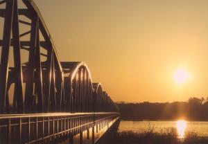まぶしく光り輝いている太陽とオレンジ色に染まった空、光を浴びている鉄橋の写真