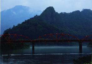 おだやかな川と、それに掛かる赤い橋に霧がかかっている写真