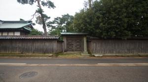中央に門がありその両脇に木製の塀が伸びている石井家住宅御小休所御門の外観写真