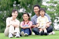緑の芝生の上に座るお母さん、女の子、隣にはお父さんの膝に座る男の子と仲の良い家族の集合写真
