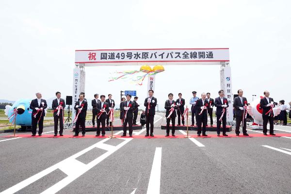 新たに整備された水原バイパスの道路の上で、国道49号水原バイパス全線開通記念セレモニーが開催され、国会議員などがテープカットを行う様子