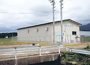 2本の電柱の奥の白い外壁の大室取水場の写真