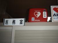 「医務室」と書かれた札が設置されており、右横に赤いバッグが置かれている写真
