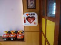 壁際に3台の子供用の車の乗り物が置いてあり、壁には「AED」が設置されている写真