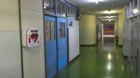 長い廊下と水色の教室入り口があり、壁側には「AED]が設置されている写真